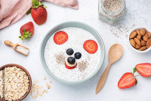 Fototapeta Zdrowe śniadanie dla dzieci z zabawną sztuką jedzenia twarzy. Budyń Chia z mlekiem migdałowym, owsem i jagodami. Widok z góry