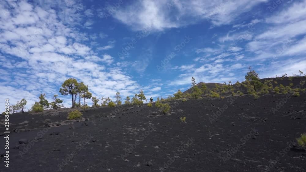 A hiker in the distant hikes up a volcano beneath a beautiful cloudy sky A hiker in the distant hikes up a volcano beneath a beautiful cloudy sky