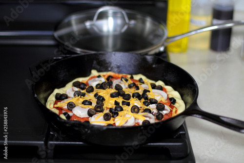 Pizza with pepperoni, mushrooms, and black olives ready to bake in the oven.