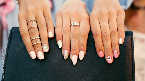 Crop of girls showing her stylish manicure, holding thair fingers on black leather handbag. Different design of manicure after beauty salon. Female hands in accessories and rings. Concept of beauty.
