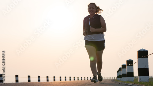 Overweight Asian women jogging in the street in the early morning sunlight. concept of losing weight with exercise. with copy space.