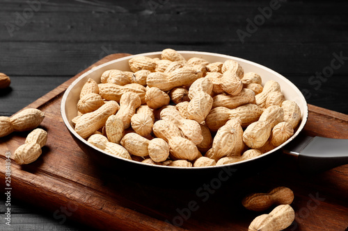 Roasted peanuts in a frying pan on the kitchen board on a wooden table. home serving. Place for text.