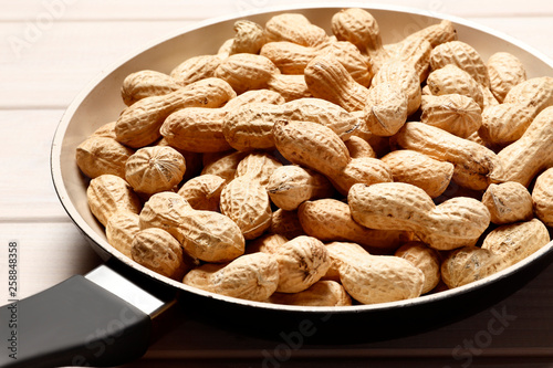 Frying pan full of fried tasty peanuts on a white wooden background with place for text. Close-up.