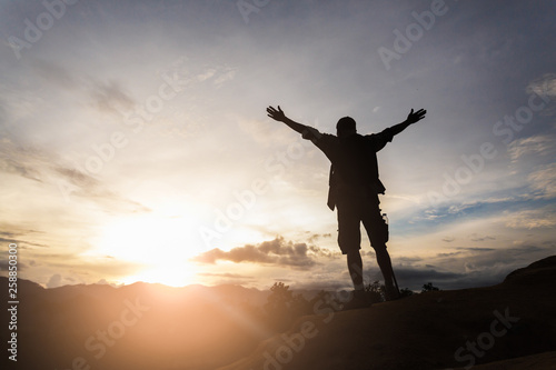 Silhouette of hiker standing on top of hill and enjoying sunrise over the valley.  The man thank God on the mountain.