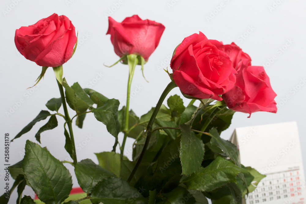 A bouquet of scarlet roses in a glass vase. Next is a calendar. On a white background.