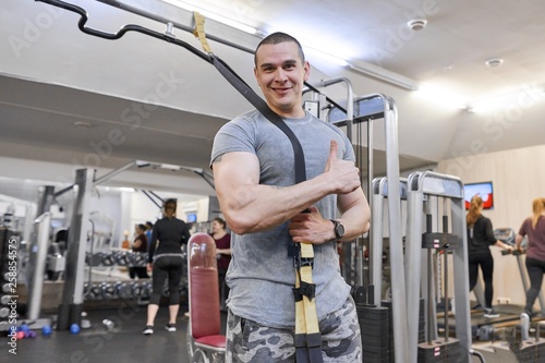 Portrait of young strong smiling muscular smiling man in gym. Male with fitness straps loops