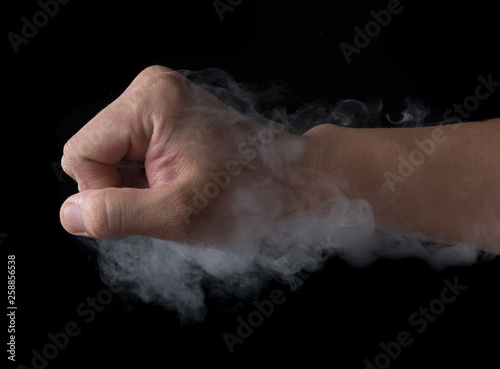 Fist punching white smoke against black background © showcake