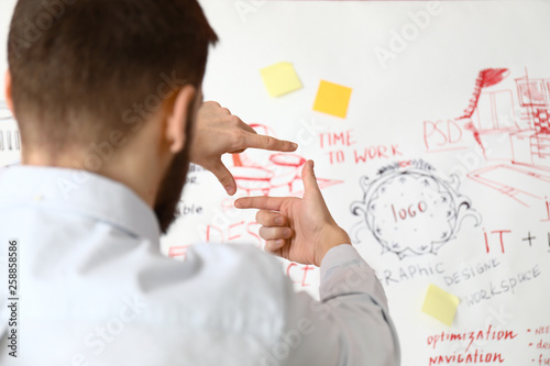 Male interior designer near big paper sheet with project plan in office