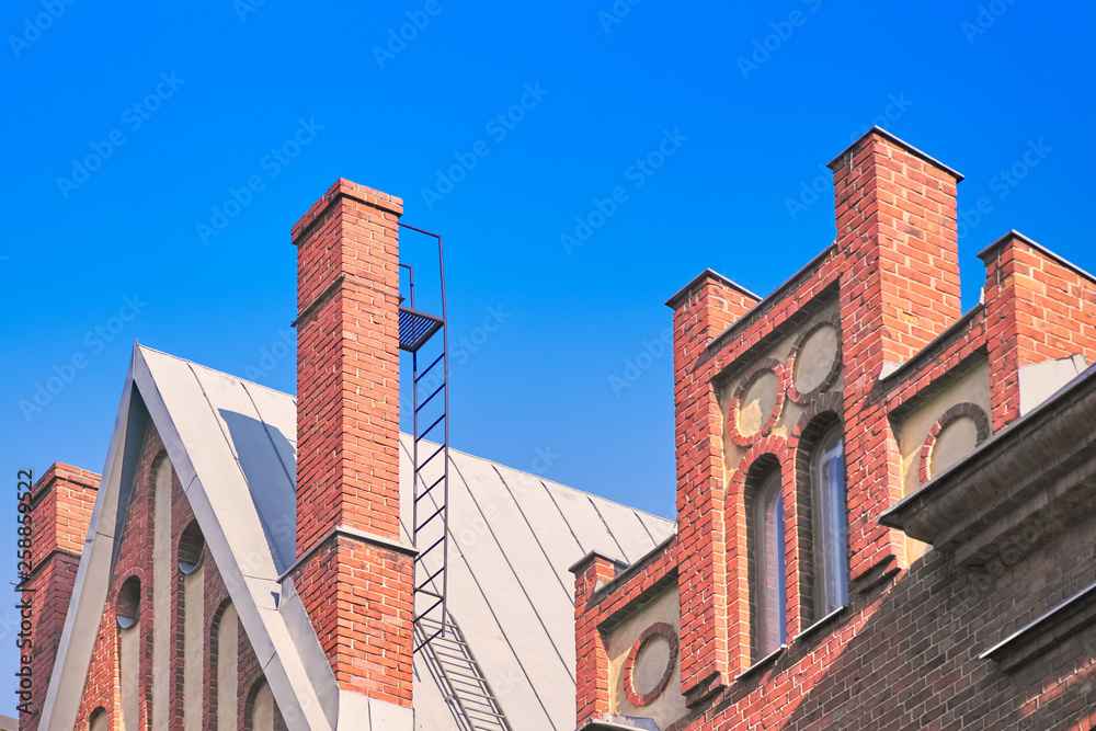 Red brick chimney on the roof, fragment of the facade of a brick building against the blue sky