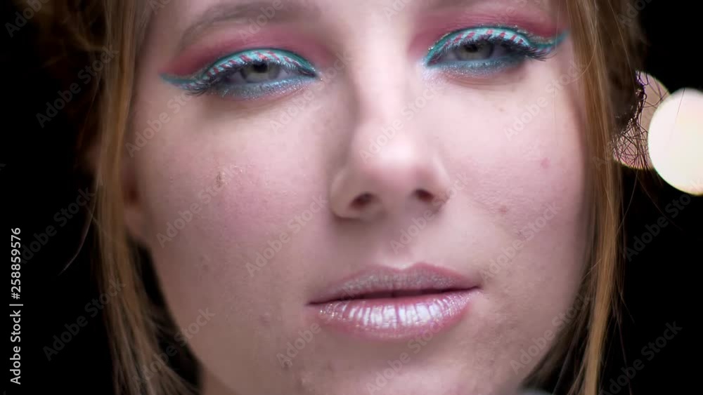 Portrait of caucasian blonde girl with multicoloured make-up smiling joyfully into camera on blurred lights background. Portrait of caucasian blonde girl with multicoloured make-up smiling joyfully into camera on blurred lights background.