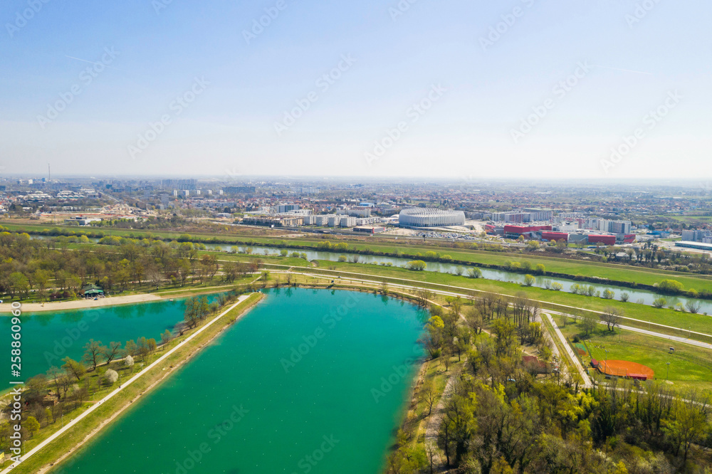 Fototapeta premium Zagreb, Croatia, Jarun lake, beautiful green recreation park area, sunny spring day, panoramic view from drone, city in background