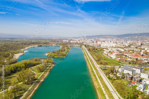 Zagreb, Croatia, Jarun lake, beautiful green recreation park area, sunny spring day, panoramic view from drone, city in background