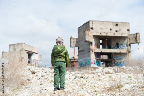 Fotografia one little lonely child in green jacket standing on ruins of destroyed buildings