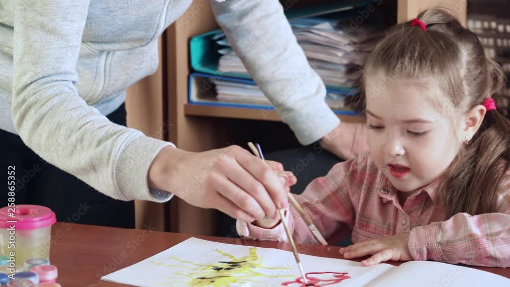 Teacher draws with little girl watercolor paints in early development school Teacher draws with little girl watercolor paints in early development school