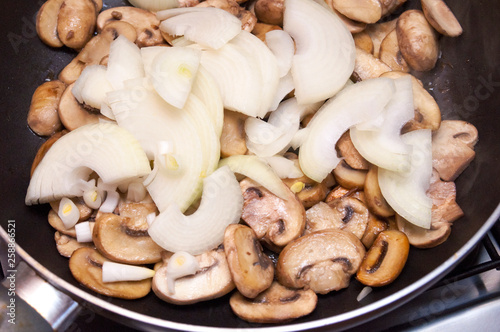 Fresh champignons and onions are fried in a pan. Top view.
