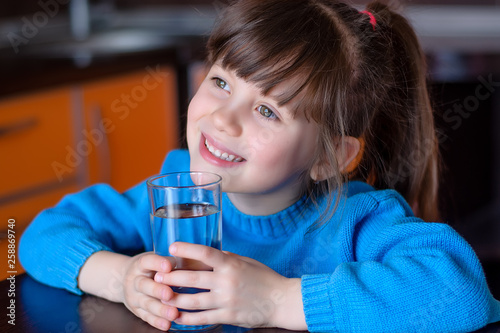 Adorable smiling little girl drinking water in kitchen. Health and beauty concept