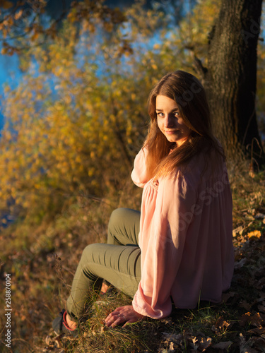 Cute girl alone sitting on the Bank of the river at sunset