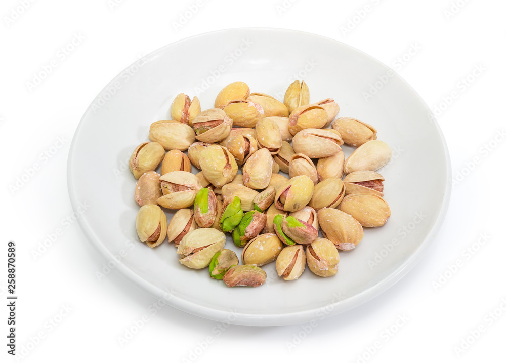 Partly peeled roasted salted pistachio nuts on the white saucer Partly peeled roasted salted pistachio nuts on the white saucer