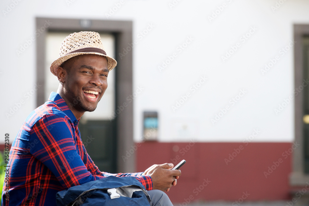 Side of handsome young african american man smiling with cellphone outdoors