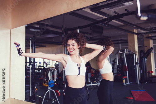 Joyful curly brunette fitness woman dancing over mirror background