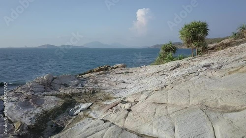 Aerial: a forward very low altitude flight slighly over white rocky hill until revealing the ocean and an island and then the drone slowly rises its altitude. photo