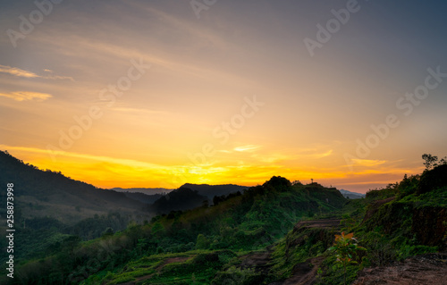 Beautiful nature landscape of mountain range with sunset sky and clouds. Mountain valley in Thailand. Scenery of mountain layer at dusk. Tropical forest. Natural background. Orange and golden sky.