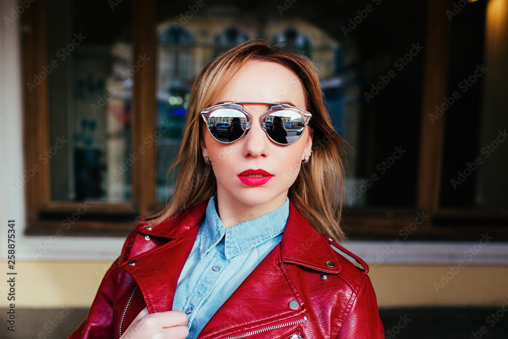 Fashion portrait of pretty young woman in leather jacket and sunglasses posing in city Fashion portrait of pretty young woman in leather jacket and sunglasses posing in city