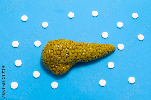 3D anatomical model of pancreas gland is on blue background surrounded by white pills as ornament polka dots. Medical concept by pharmacological tableted treating of pancreas disease, pharmacotherapy