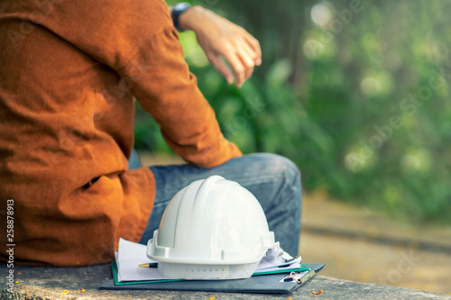 The while wearing protective equipment safety helmet at construction site and Engineer or Architect sitting and wait partner for work present project.