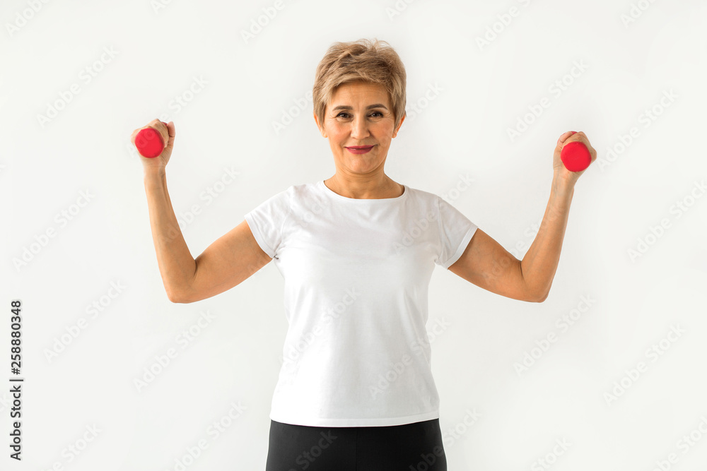 stylish elderly woman in age stands playing sports with dumbbells on a white background stylish elderly woman in age stands playing sports with dumbbells on a white background