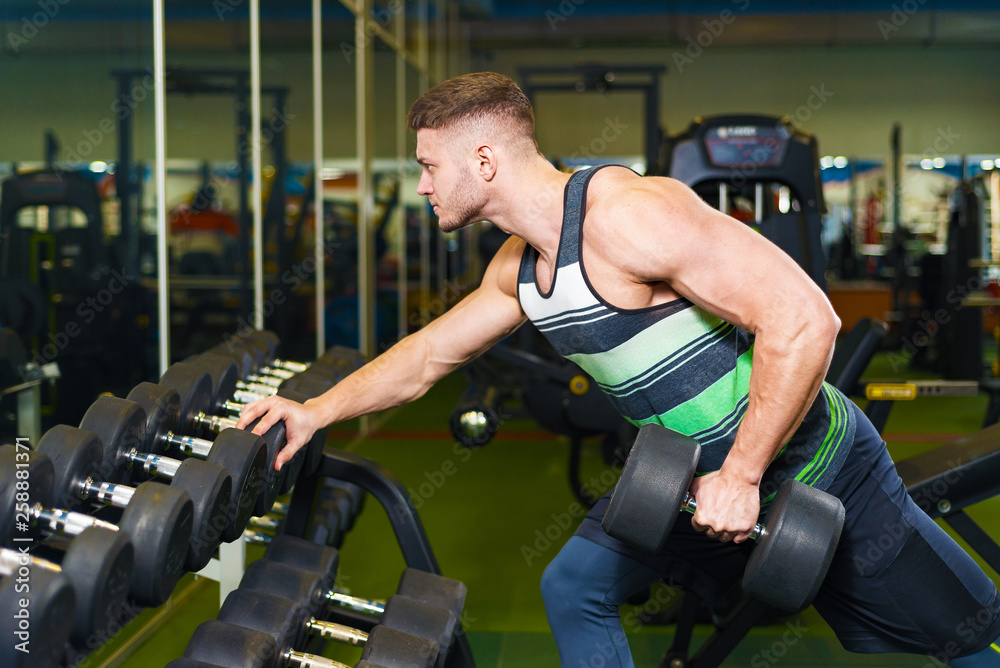 muscular man training in the gym. young guy picks up a dumbbell near the mirror. muscular man training in the gym. young guy picks up a dumbbell near the mirror.