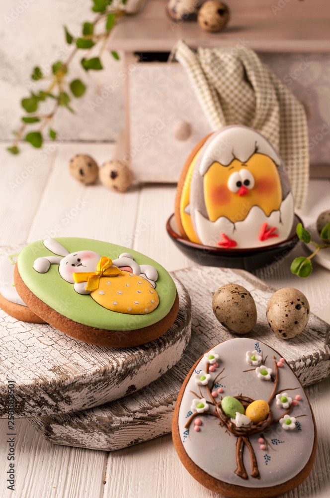 easter cookies with painted easter bunny and chicken in bowl near quail eggs, decorative sideboard and napkin on wooden surface