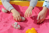 The child plays with his hands in the pink sand