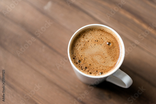 black coffee with foam in a mug on a wooden background
