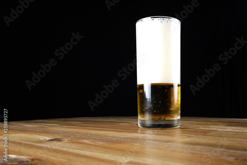 Glass of foamy beer on wooden table. Black background with copy space.