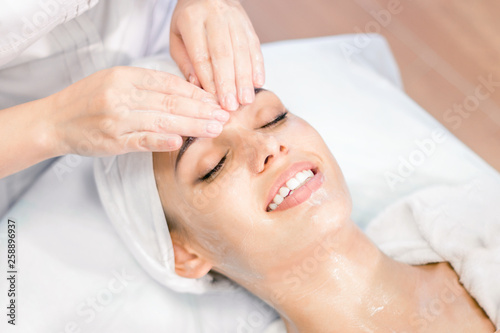 Cosmetology. The hands of a cosmetologist do a facial massage with a mask. Smiling girl on spa procedure. Facial treatment.