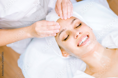 Cosmetology. The hands of a cosmetologist do a facial massage with a mask. Smiling girl on spa procedure. Facial care concept.