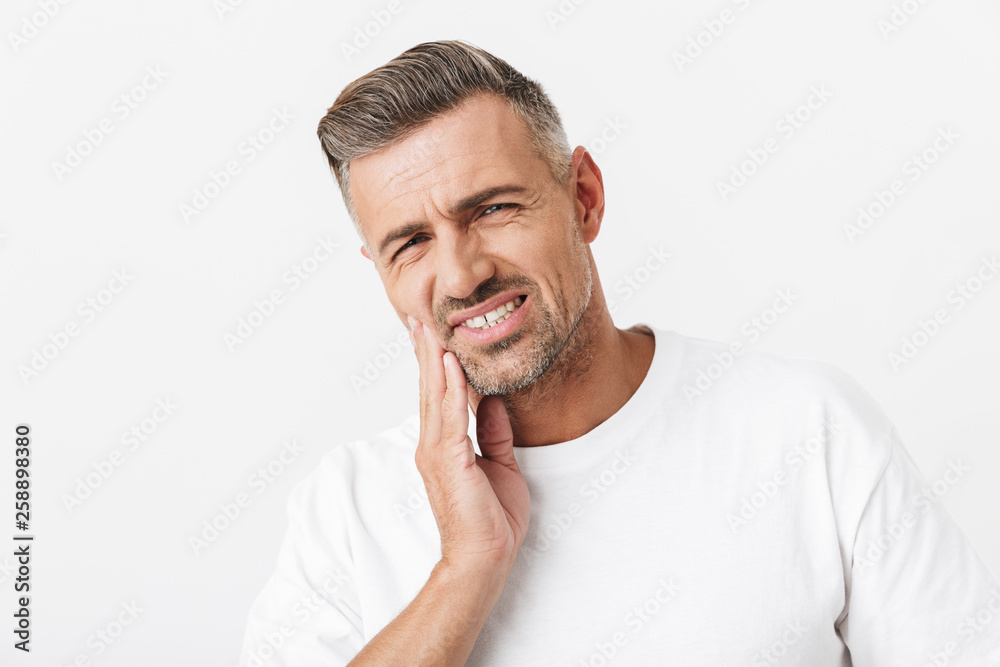 Image of unshaved man 30s with bristle wearing casual t-shirt touching his cheek and suffering from toothache