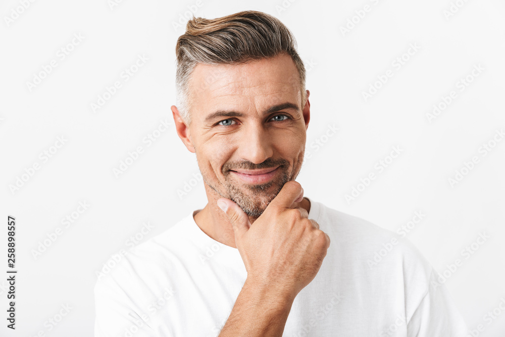 Image of optimistic man 30s with bristle wearing casual t-shirt smiling and touching chin Image of optimistic man 30s with bristle wearing casual t-shirt smiling and touching chin