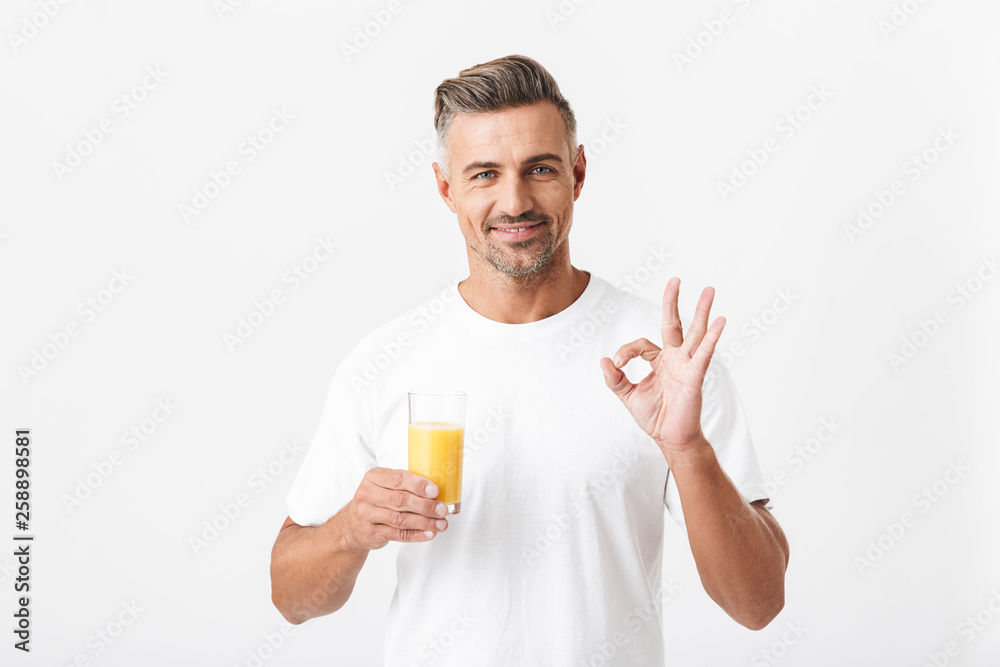 Image of attractive man 30s with bristle wearing casual t-shirt showing ok sign while holding glass of orange juice Image of attractive man 30s with bristle wearing casual t-shirt showing ok sign while holding glass of orange juice