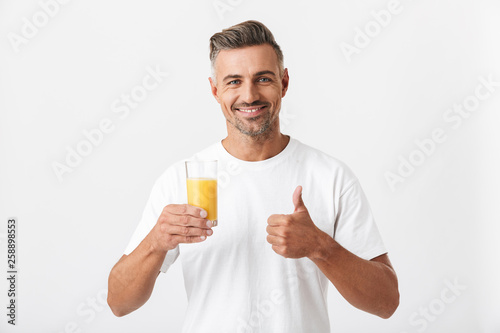 Image of european man 30s with bristle wearing casual t-shirt holding glass of orange juice