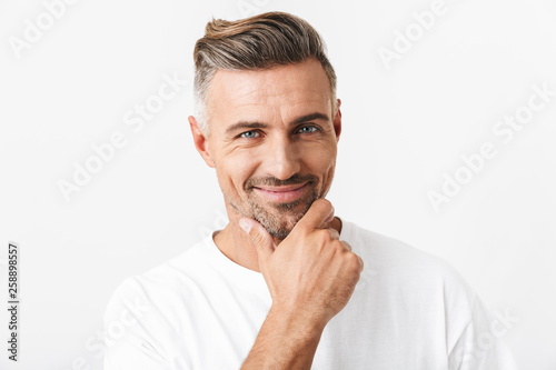 Image of optimistic man 30s with bristle wearing casual t-shirt smiling and touching chin
