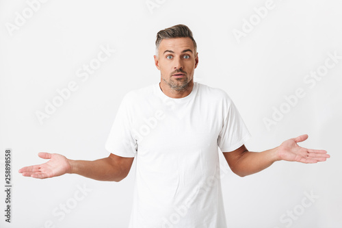 Image of puzzled man 30s with bristle wearing casual t-shirt throwing up hands