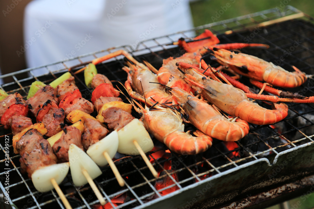 Roasted prawns and pork with vegetable kebabs on barbecue grilling stove.