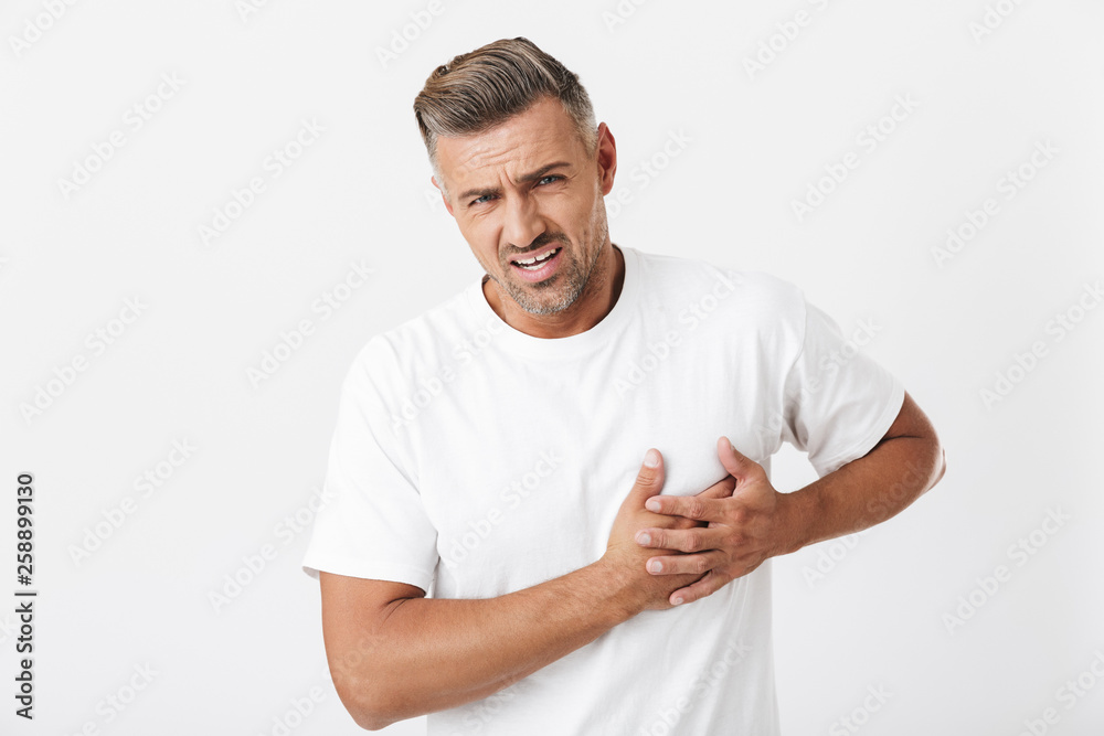 Image of frowning man 30s with bristle wearing casual t-shirt touching his heart because of pain Image of frowning man 30s with bristle wearing casual t-shirt touching his heart because of pain