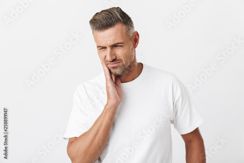 Image of muscular man 30s with bristle wearing casual t-shirt touching his cheek and suffering from toothache © Drobot Dean