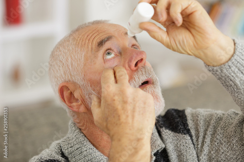 senior man dripping a red eye with eye drops photo