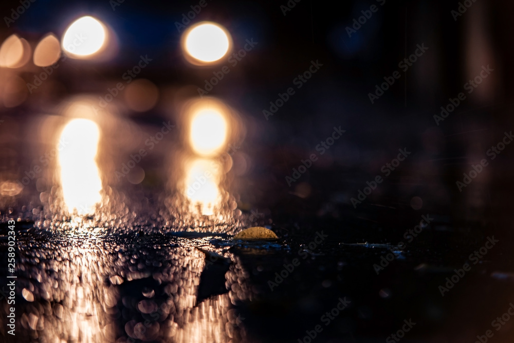 Night road blurred. Rain drops rippling in a puddle on a dark, rainy day, close up with soft selective focus . Water splashes, spills on roadway