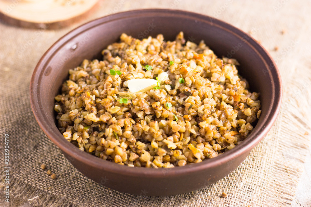 Buckwheat porridge with mushrooms on a plate. Buckwheat porridge in black casserole on wooden background closeup Buckwheat porridge with mushrooms on a plate. Buckwheat porridge in black casserole on wooden background closeup