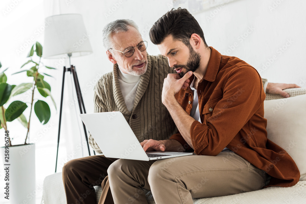 senior father looking at handsome son sitting with laptop senior father looking at handsome son sitting with laptop